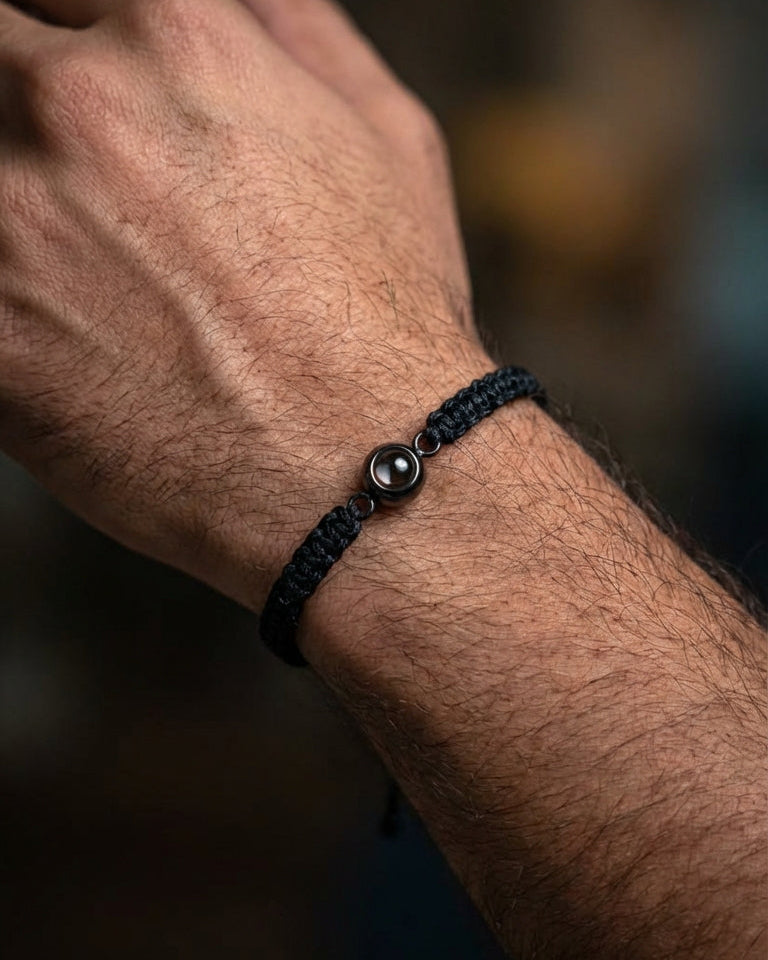 Close-up of a wrist wearing a black braided bracelet with a metal bead on a blurred background